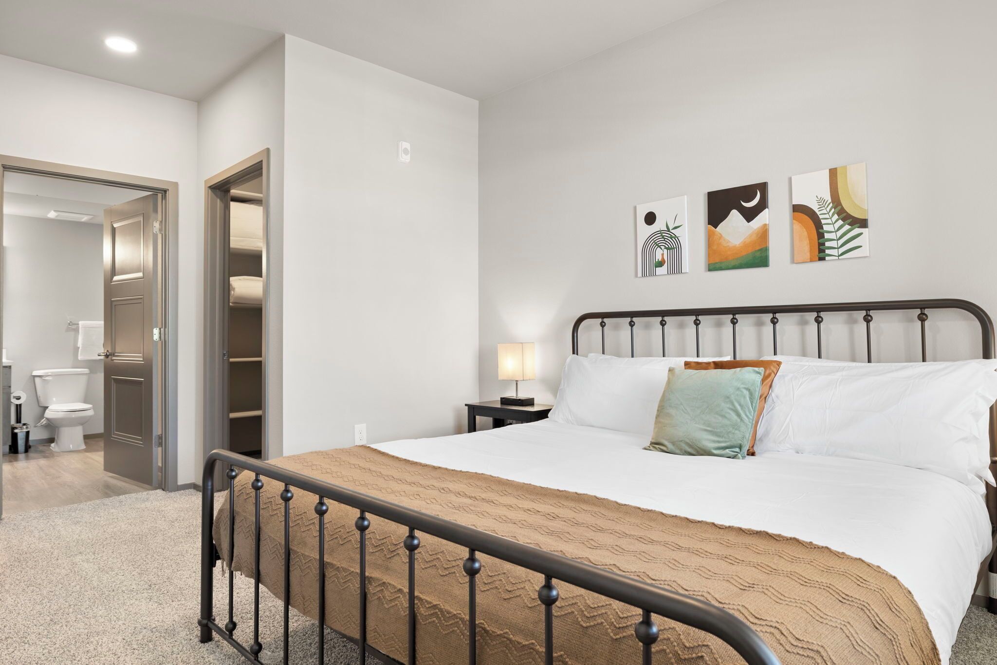 A bedroom with a bed, bedside table, lamp, and artwork on the wall.