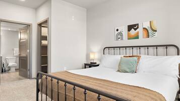 A bedroom with a bed, bedside table, lamp, and artwork on the wall.