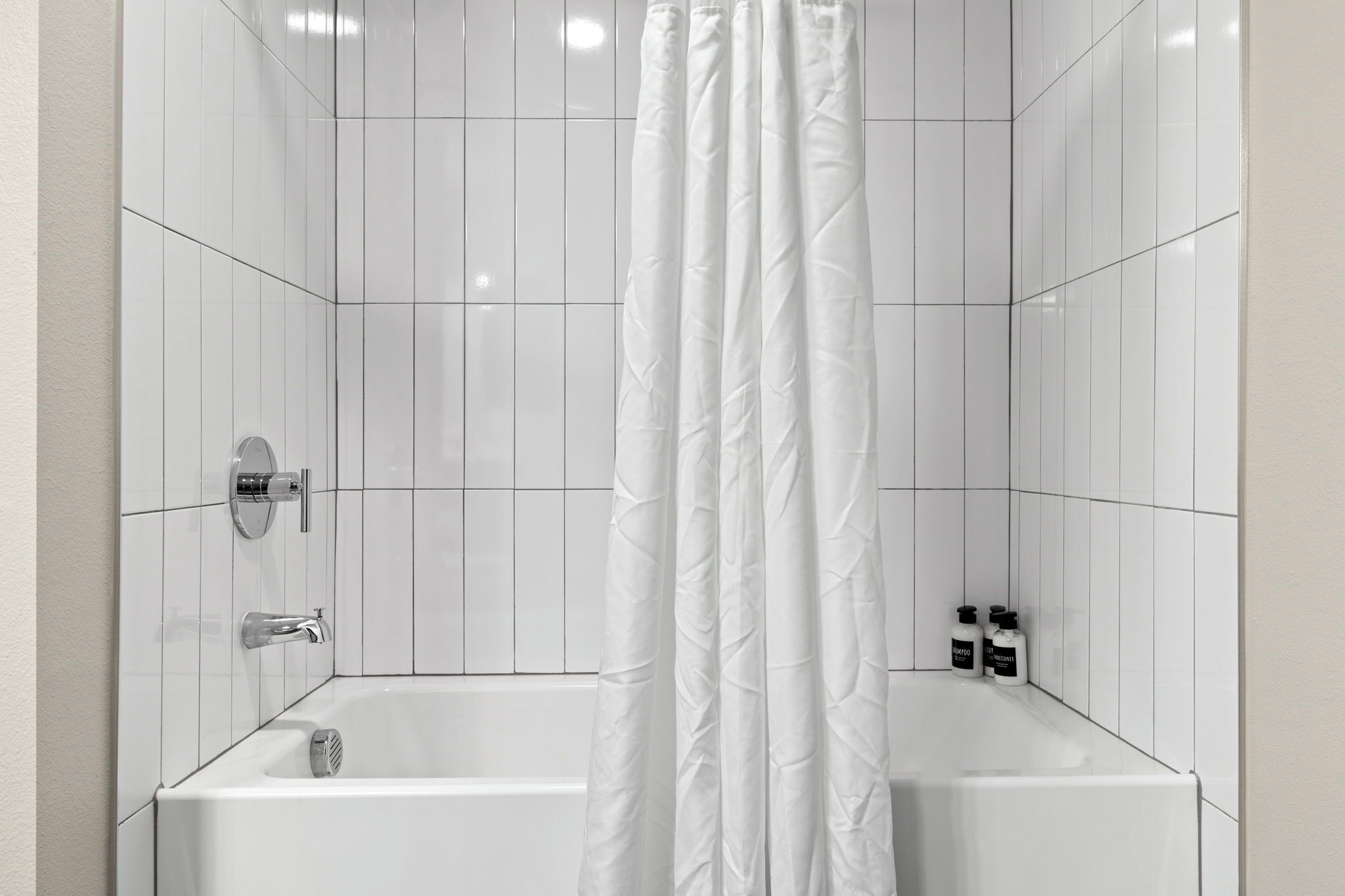 A bathroom with white tiled walls, a bathtub, a shower curtain, and two bottles of shampoo.