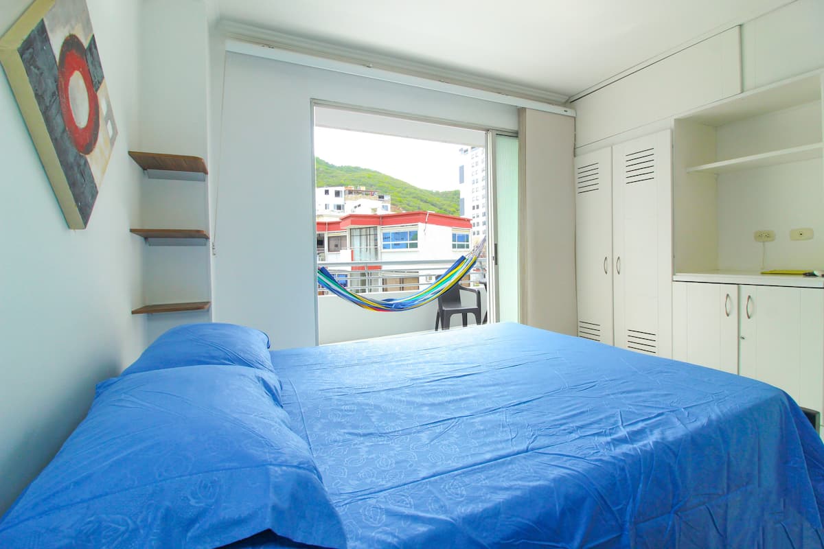 Ein Schlafzimmer mit Bett, einer Hängematte, Blick auf Gebäude und einem Balkon.