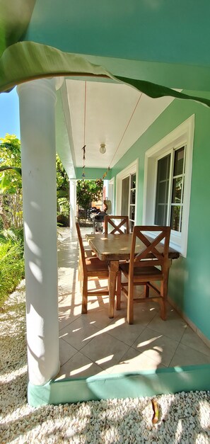 A covered patio area with a wooden table and chairs, surrounded by white pillars and a teal wall. - Charming Villa in Sosua (Sosua)