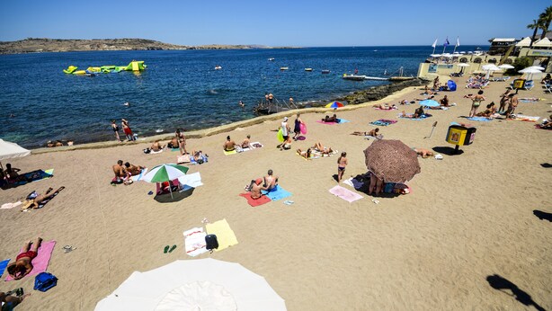Une plage où l’on peut voir des gens se prélasser au soleil, des parasols et une tour de surveillance des sauveteurs.