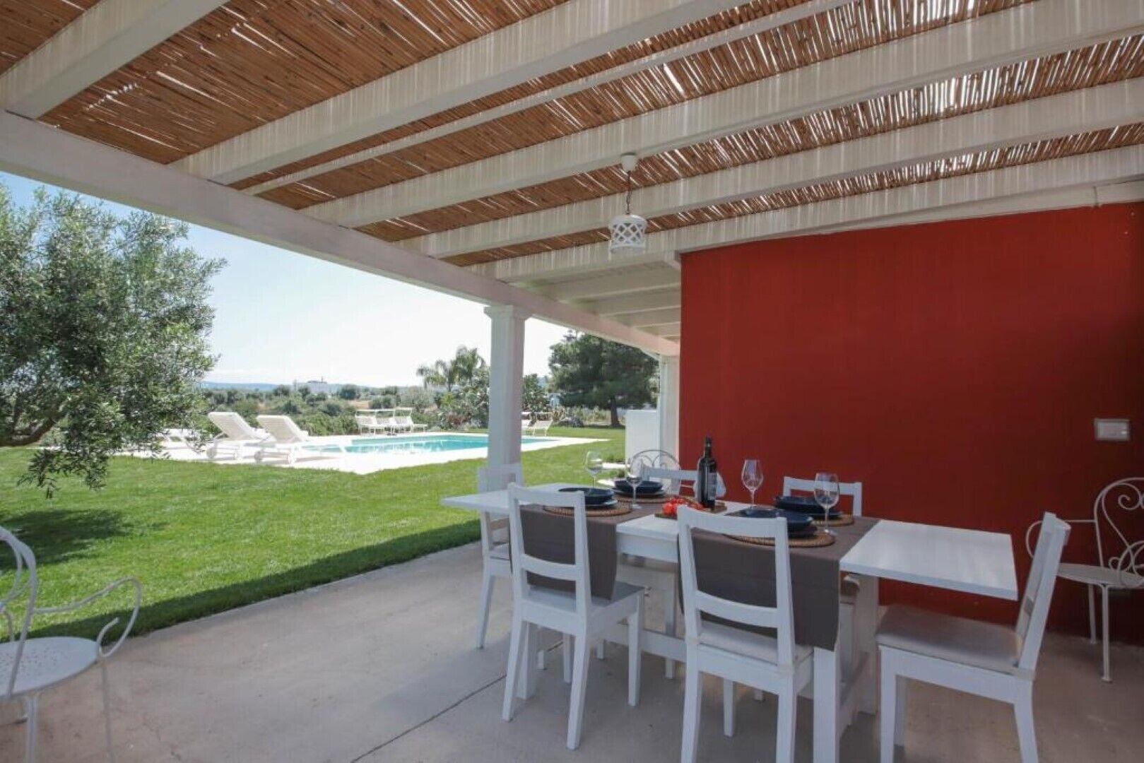 An outdoor patio with a table set for dining, overlooking a swimming pool and a grassy area.