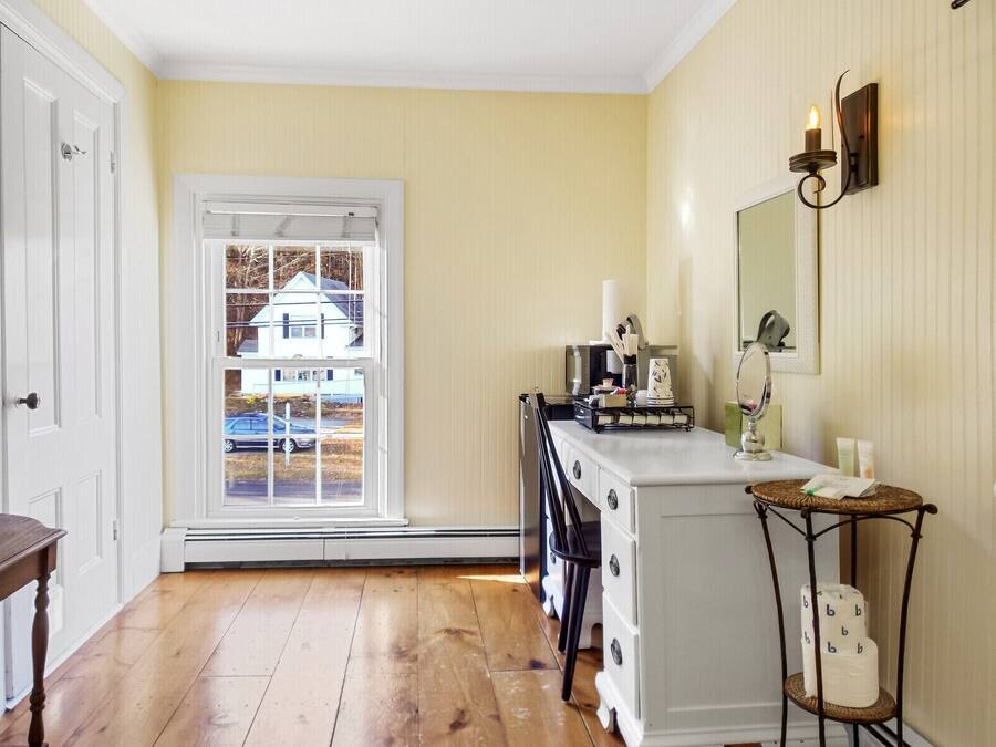 A room with a wooden floor, a white dresser, a mirror, and a window with a view of a house and parked cars.
