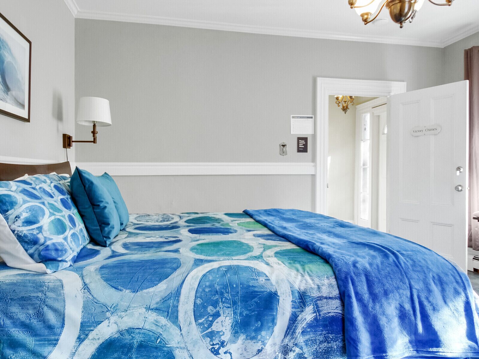 A hotel room with a bed, a nightstand, a lamp, and a door labeled "Victory Chimes".