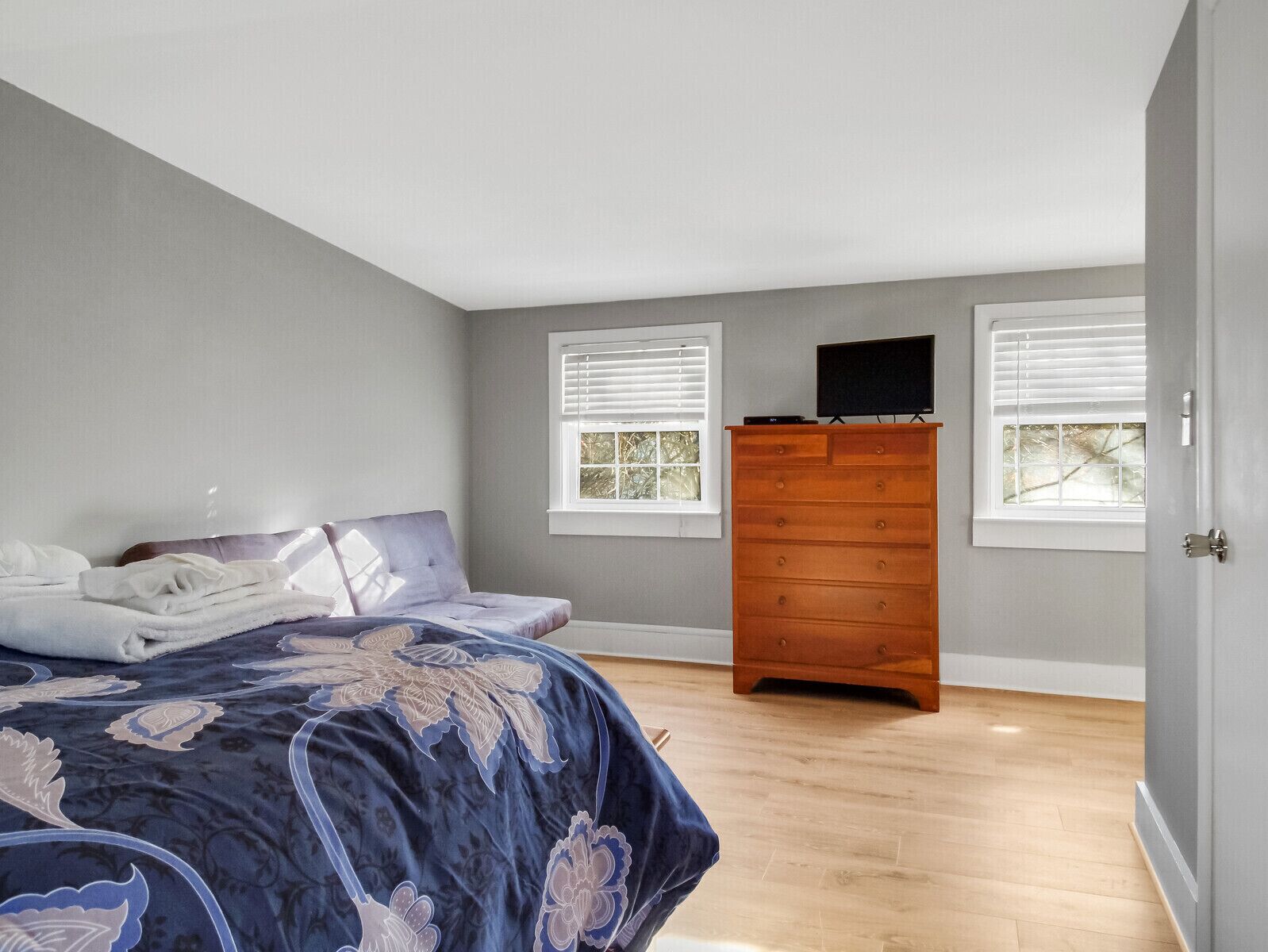 A bedroom with a bed, a dresser, and two windows with blinds.