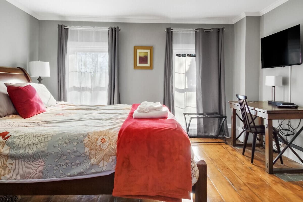 A hotel room with a bed, a desk, a chair, a television, and a picture on the wall.