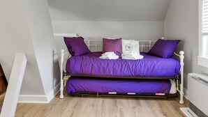 A two-level bunk bed with purple bedding, white headboard, and a white radiator on the wall. - The Thistle Inn (Boothbay Harbor)
