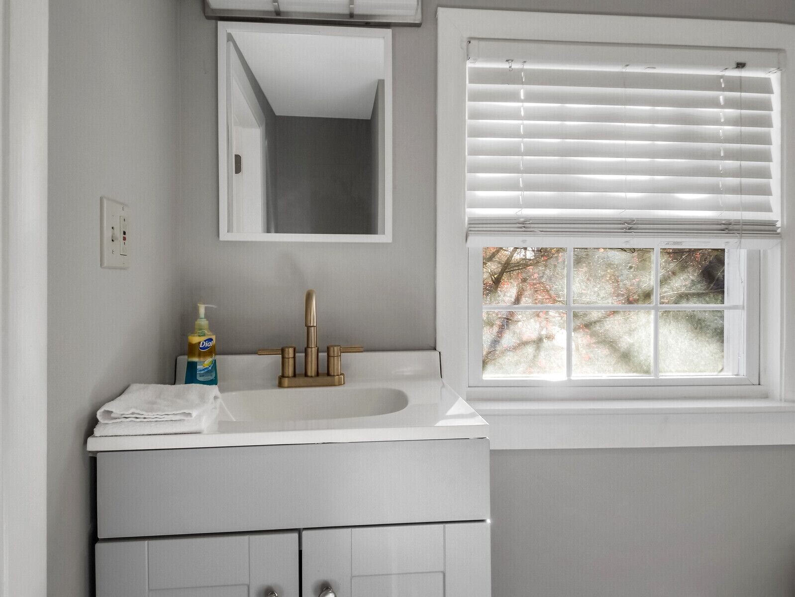 A bathroom with a white sink, a mirror above it, and a window with blinds.