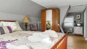 A bedroom with a bed, a nightstand, a lamp, a chair, a wardrobe, and a kitchenette.