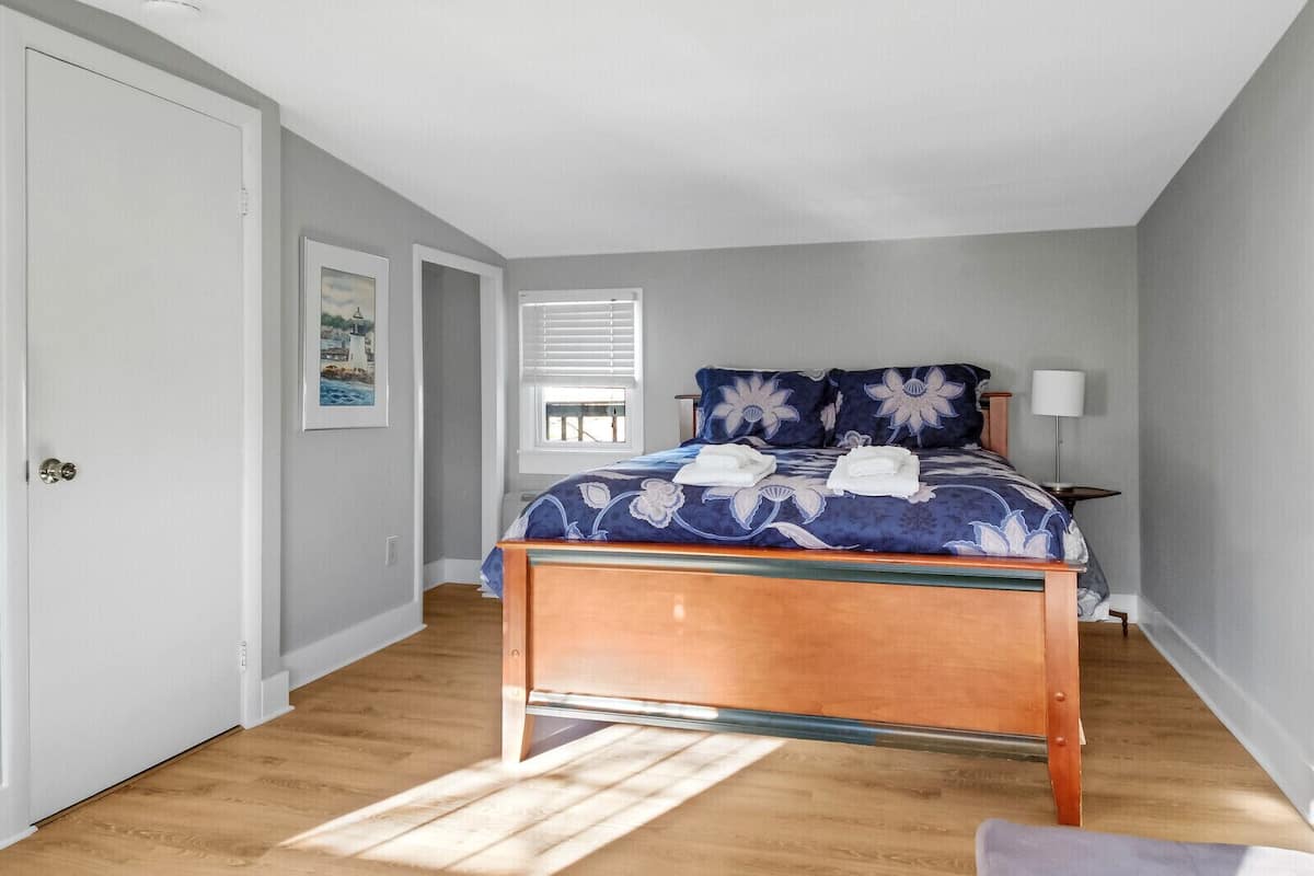 A bedroom with a bed, a nightstand, a lamp, and a window with blinds.