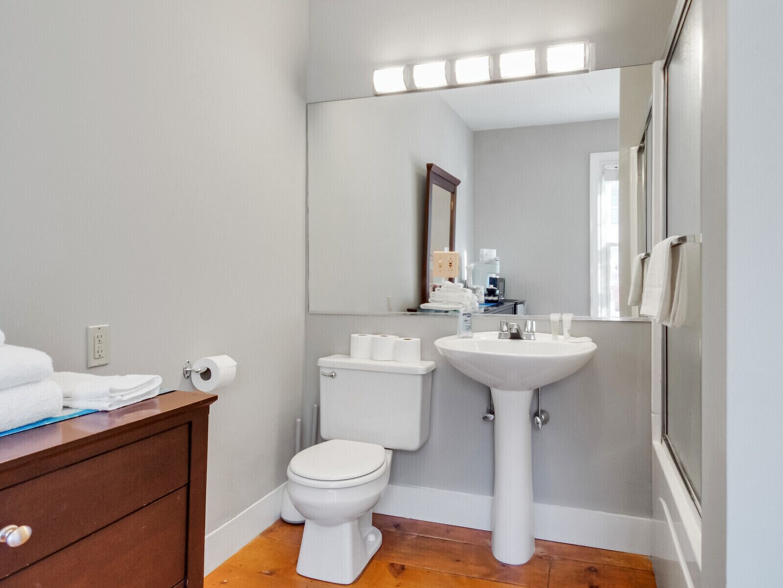 A bathroom with a toilet, sink, and mirror. There are towels on the counter and a mirror above the sink.