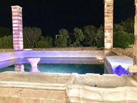 Una piscina nocturna con pilares de piedra y borde de piedra.