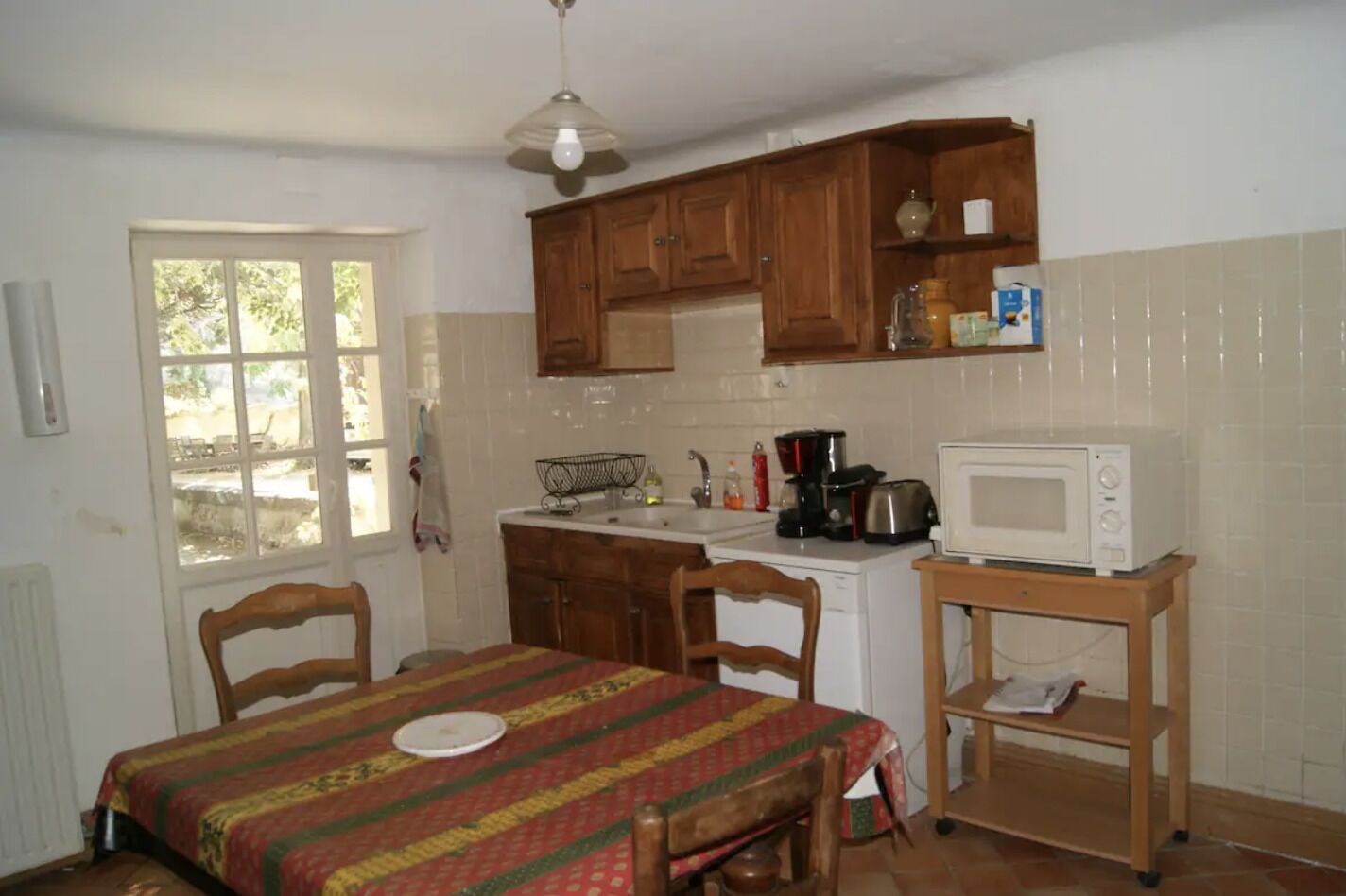 A compact kitchen with wooden cabinets, a microwave, a coffee maker, and a dining table with chairs.