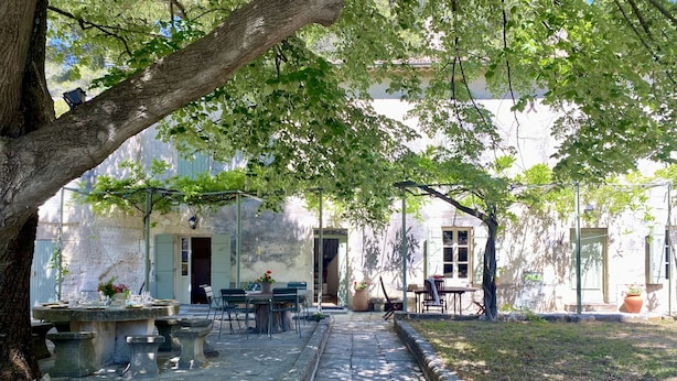 Ein gepflasterter Weg führt zu einem Innenhof mit Außenbestuhlung und einem Gebäude im Hintergrund.