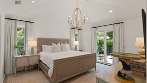 A spacious bedroom with a large bed, two bedside tables, a chandelier, and a view of the outdoors. - Quaint Cottage near the village with pool (St Simons Island)