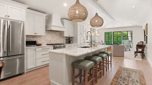 A modern kitchen with white cabinetry, stainless steel appliances, a large island with bar stools, and large wicker pendant lights. - Quaint Cottage near the village with pool (St Simons Island)