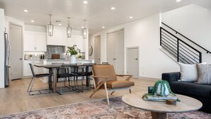 A modern kitchen with white cabinets, a dining area with a round table and chairs, a black sofa, and a staircase. - Lagoon Vibes: Desert Color Lagoon + Beaches (St George)