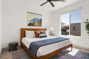 Ein modernes Schlafzimmer mit einem großen Bett, einem Deckenventilator, einem Fenster mit Blick und einem Bild an der Wand.