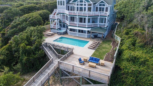Uma casa grande, de vários andares, com piscina, deck e móveis de exterior.