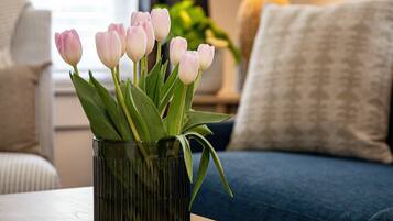 Una mesa de centro de madera con un jarrón de tulipanes rosados en un recipiente de vidrio texturizado.