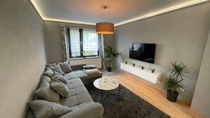 A modern living room with a grey sectional sofa, a round coffee table, and a TV mounted on the wall. - Modernes Reihenhaus mit Garten (Magdeburg)