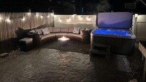 Eine Terrasse im Freien mit Whirlpool, gebogenem Sofa und Lichterketten.