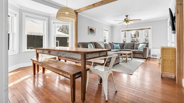 Ein geräumiges Wohnzimmer mit einem Holzesstisch, weißen Stühlen und einer Couch mit Kissen.