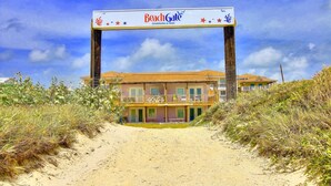 A beachfront property named BeachGate with a sandy path leading to a building with balconies. - Beachgate Condo Suites And Hotel 231+233 2 Bedroom Condo (Port Aransas)