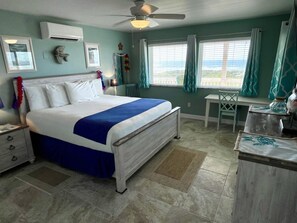A bedroom with a bed, a desk, and a chair. There is a window with curtains and a view of the outside. - Beachgate Condo Suites And Hotel 231+233 2 Bedroom Condo (Port Aransas)