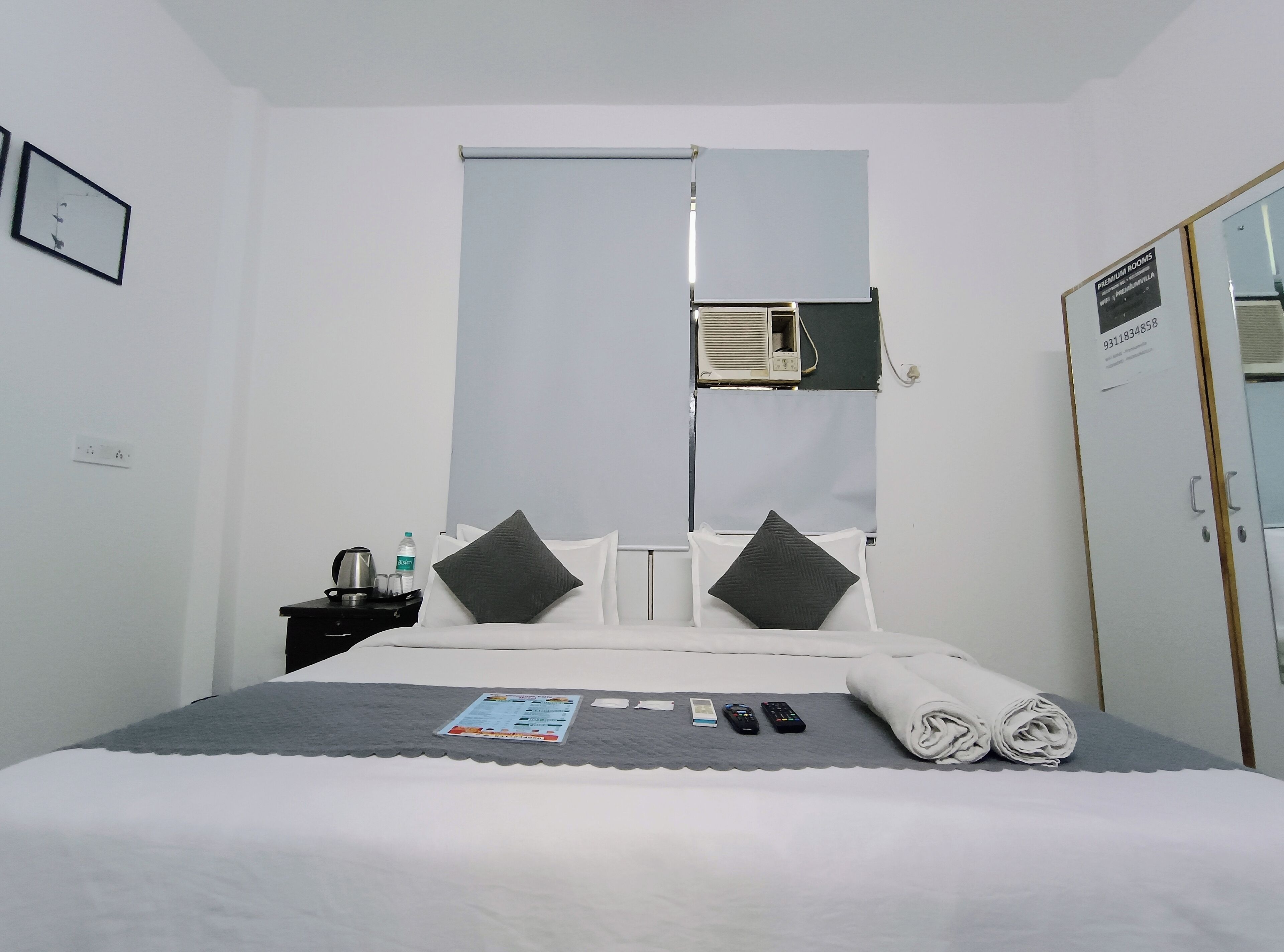 Una habitación de hotel con cama, mesita de noche, botella de agua, control remoto y toalla doblada.