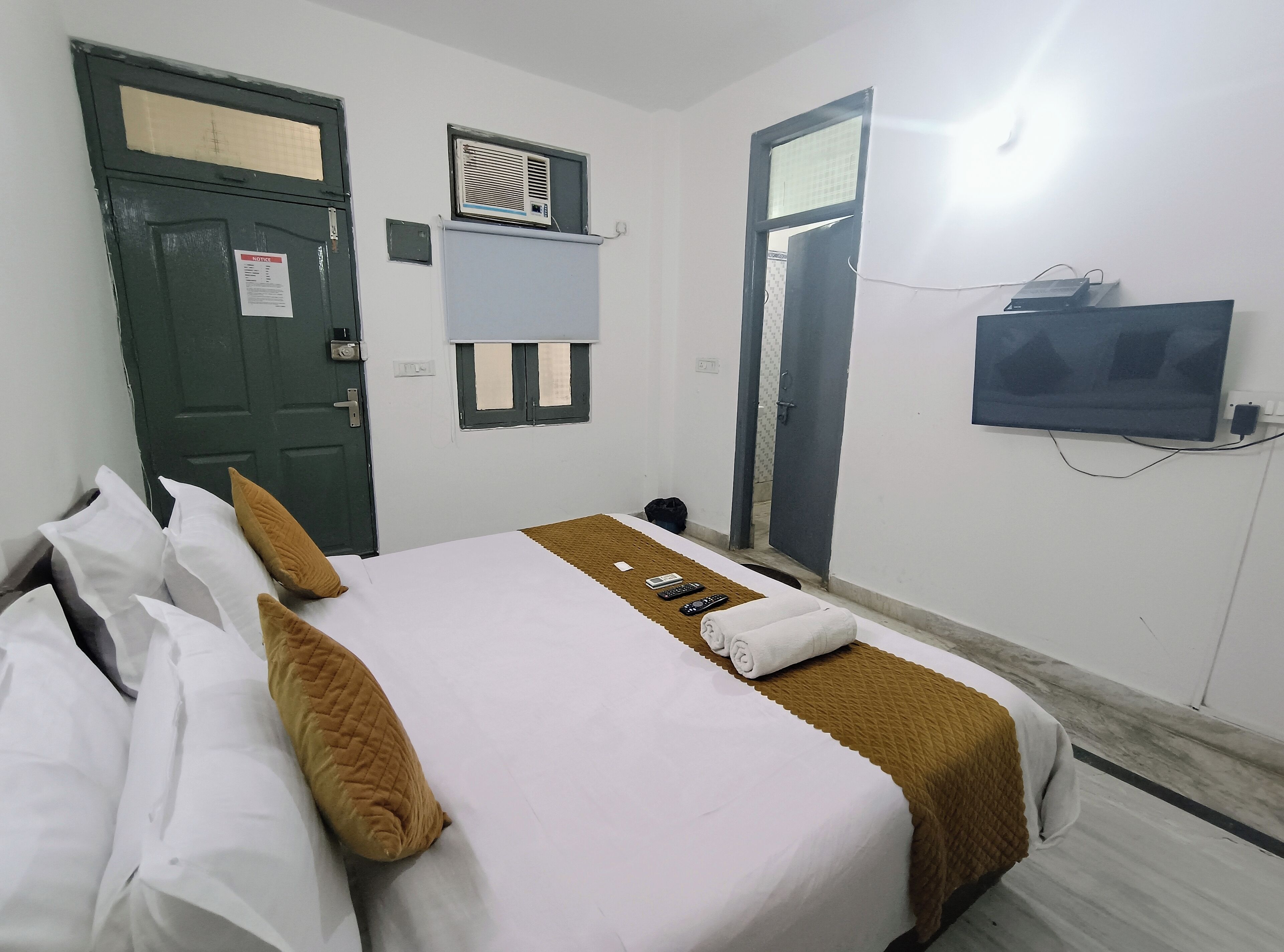 A hotel room with a bed, a TV mounted on the wall, and a door with a notice on it.