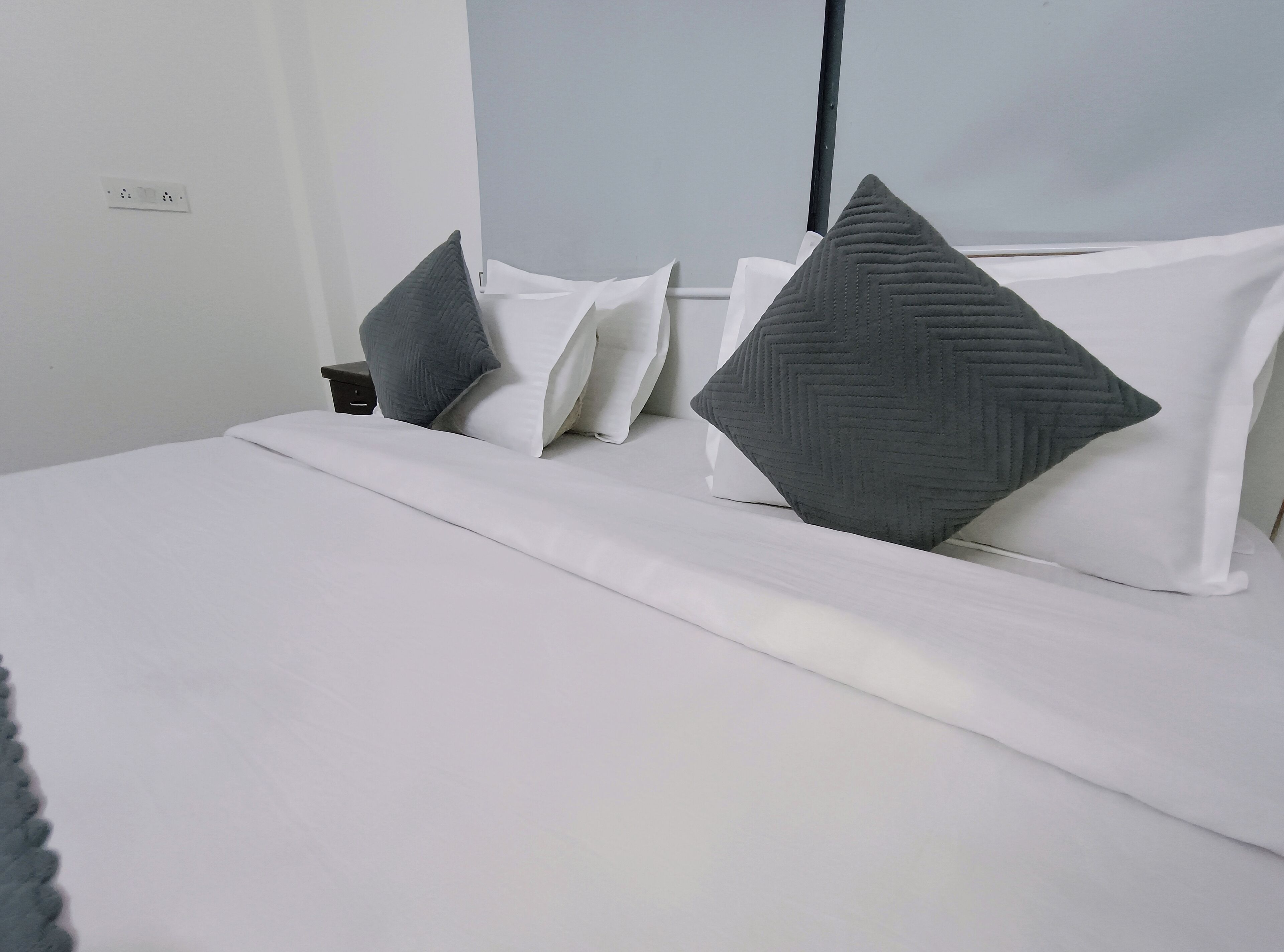 A neatly made bed with white bedding and two gray pillows.