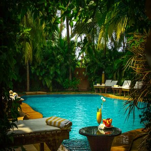 A pool area with lounge chairs and a table with a drink and flowers. - Papa Jolly Eco Resort - Near Morjim Beach (Morjim)