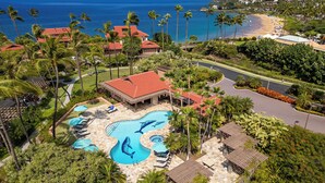 Un resort con piscina que presenta murales de delfines, rodeado de palmeras y vistas al océano.