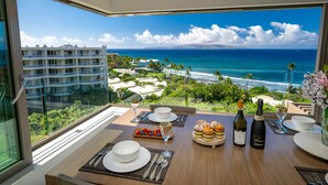 Una mesa de comedor con vista al océano, un balcón y un edificio al fondo.