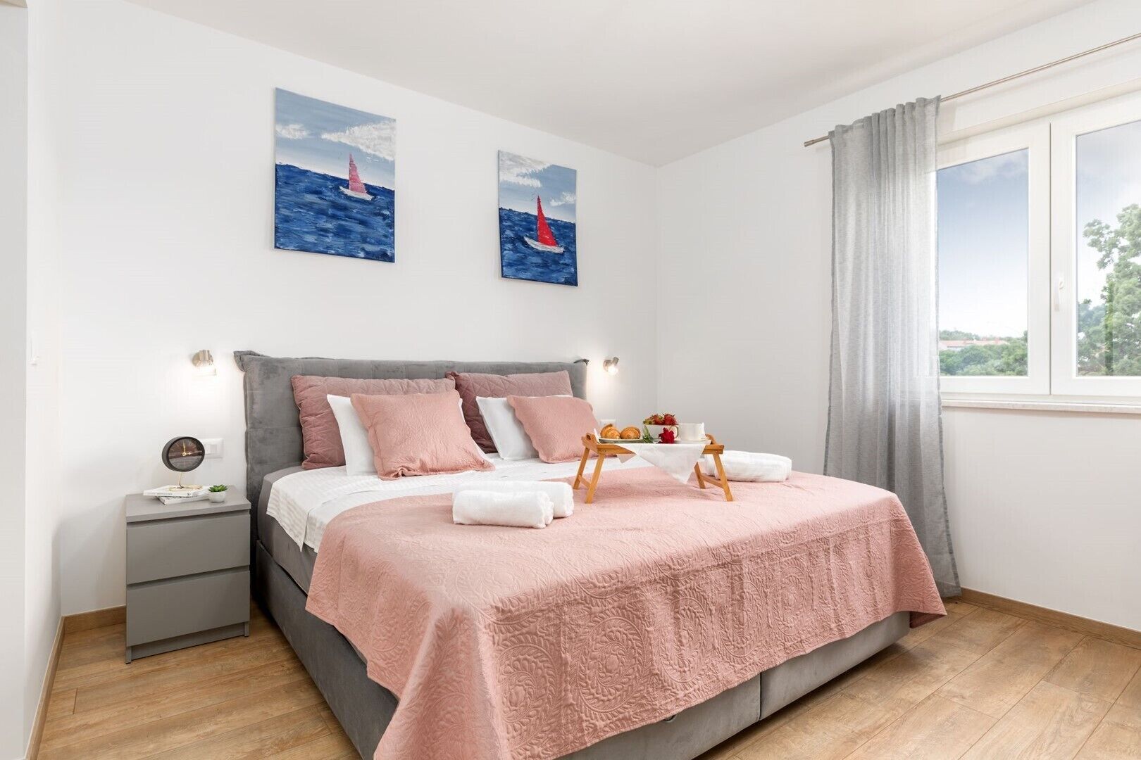 A bedroom with a bed, bedside tables, a window with curtains, and two wall paintings.