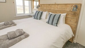 Un dormitorio con cabecera de madera, una cama grande con ropa blanca, almohadas a rayas y dos lámparas de noche.