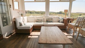 Un área de estar al aire libre acogedora con un sofá de mimbre, una mesa de madera y sillas de mimbre, con vistas a un paisaje pintoresco.
