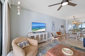 Sala de estar com televisão, ventilador de teto, área de refeições e vista para o mar.
