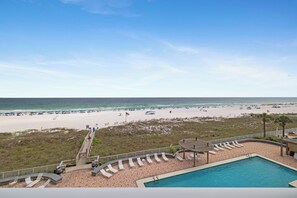 Vista da praia a partir de um resort, com piscina, espreguiçadeiras e um calçadão.