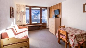 A room with a bed, a desk, a chair, a table, a TV, and a window with a view of buildings. - 100m from resort center, 4th floor, balcony, tv, ski locker, 24m², Tignes (Tignes)