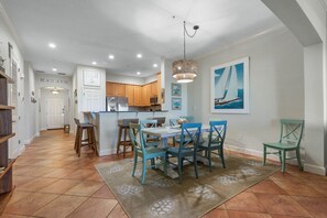 A modern kitchen with wooden cabinets, a central island, and a dining area with blue chairs and a white table.