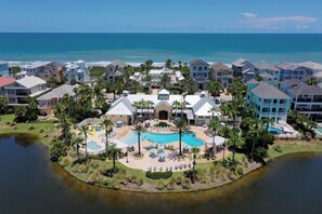 A resort with a central pool, multiple buildings, and a view of the ocean.