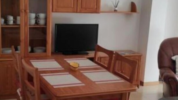 A dining area with a wooden table and chairs, a television, and wooden cabinets. - Piso As Rodas (Vilanova de Arousa)