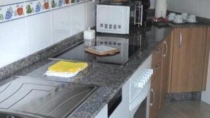 A kitchen with wooden cabinets, a granite countertop, a built-in oven, and a microwave. - Piso As Rodas (Vilanova de Arousa)