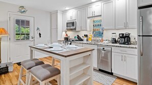 Una cocina moderna con armarios blancos, un refrigerador de acero inoxidable y una isla central con taburetes.