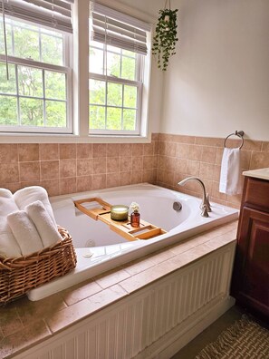 Une salle de bain avec une baignoire, un plateau en bois avec des bougies, un panier en osier rempli de serviettes et une plante suspendue.
