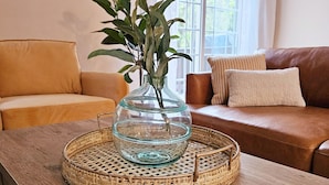 A wooden table with a glass vase containing green leaves, placed on a woven tray. - Creekside Orchards townhome in the heart of Chambersburg! (Chambersburg)