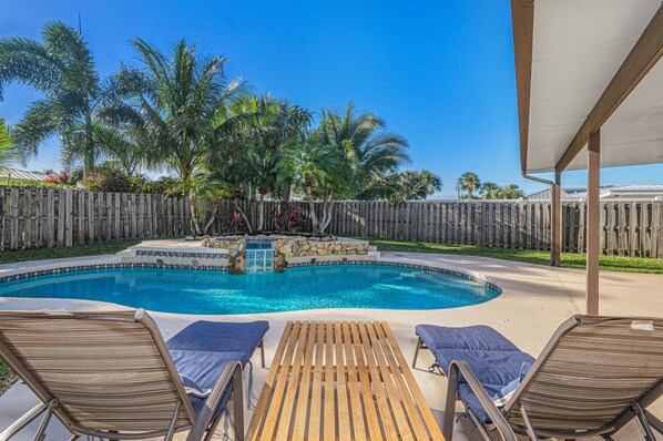 A swimming pool with wooden lounge chairs and a wooden fence. - Pink Flamingo Island Oasis (Fort Pierce)